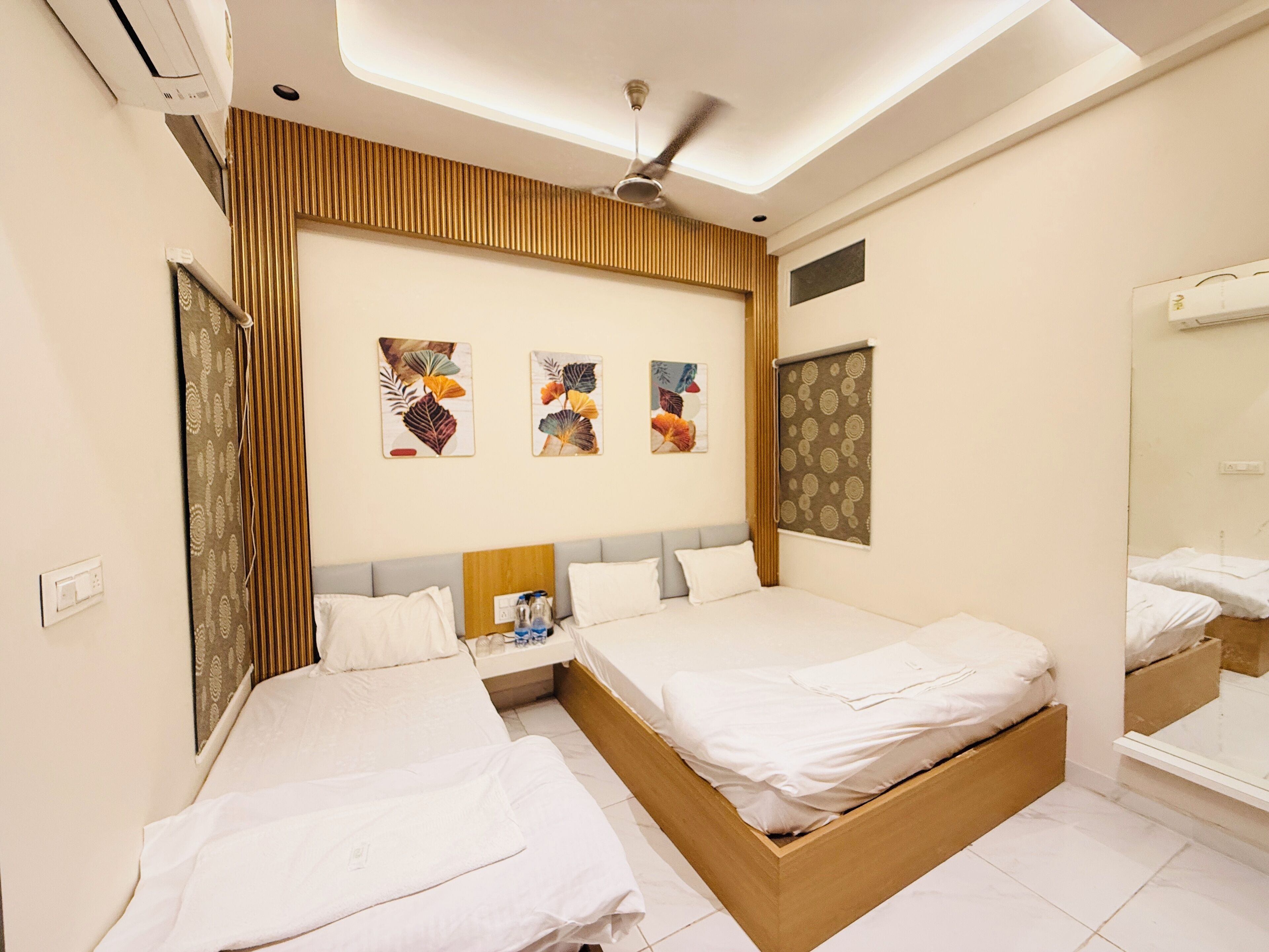 Une chambre d’hôtel avec deux lits, un ventilateur de plafond, des œuvres d’art accrochées au mur et un grand miroir.
