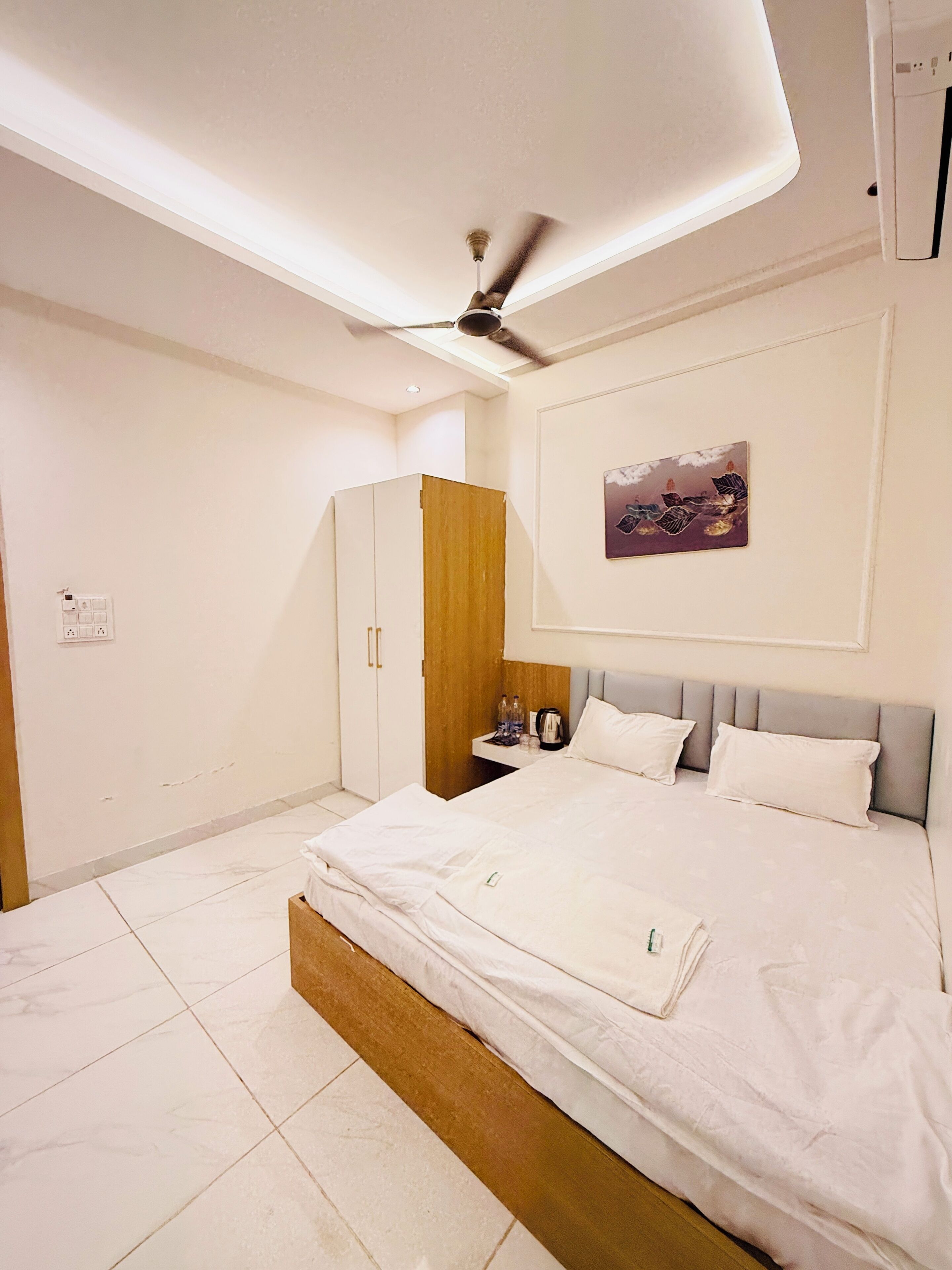 A modern bedroom with a bed, a wardrobe, a ceiling fan, a nightstand, and a wall-mounted artwork.