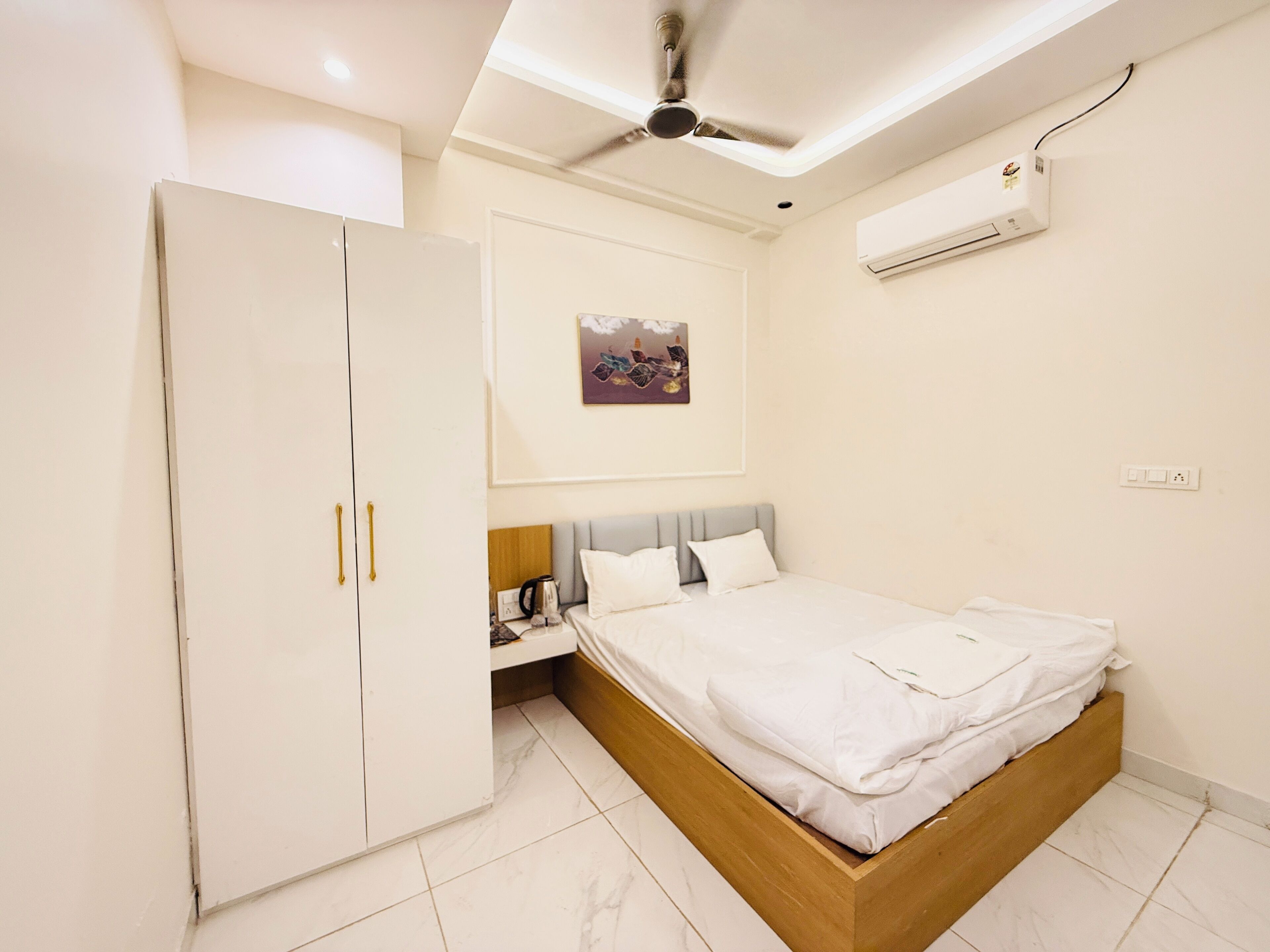A bedroom with a bed, wardrobe, ceiling fan, air conditioning unit, and a wall-mounted picture.