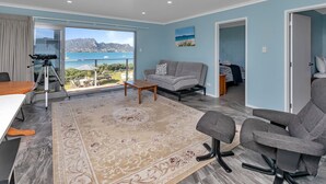 A spacious living room with a balcony, a dining area, and a bedroom. - The Lookout Waterfront Apartment at Harbour Lights (One Tree Point)