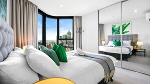 Et moderne hotelværelse med en stor seng, en dobbeltseng og udsigt over byen, adskilt af glas.