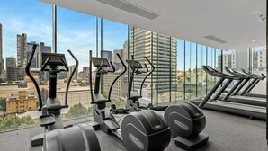 Et fitnesscenter med træningsudstyr og løbebånd, store vinduer med udsigt over byen.