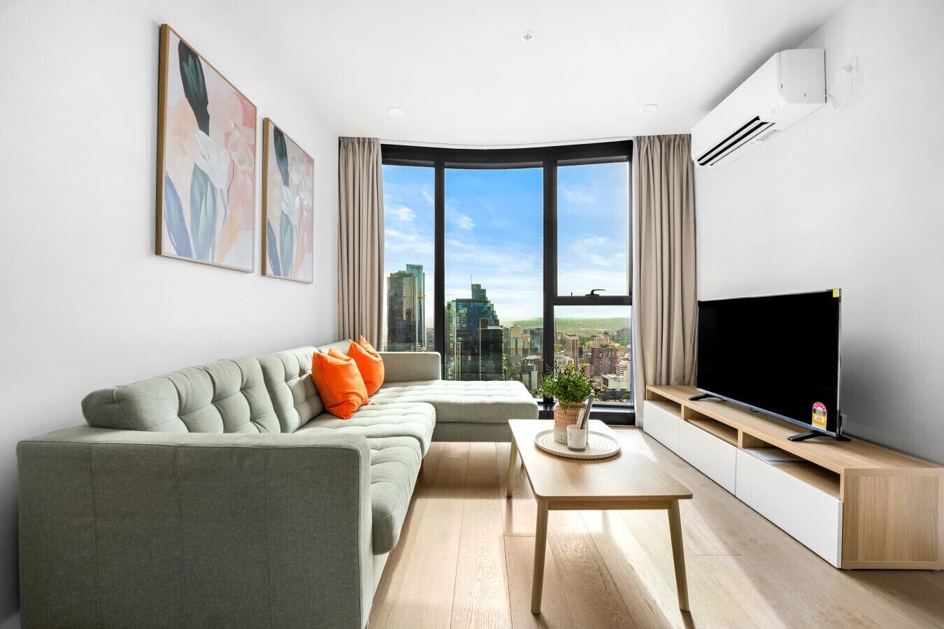 Ein modernes Wohnzimmer mit Sofa, Couchtisch, Flachbildfernseher und einem großen Fenster mit Blick auf die Stadt.