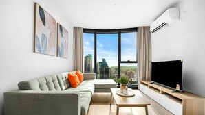 En moderne stue med sofa, sofabord, fladskærms-tv og et stort vindue med udsigt over byen.