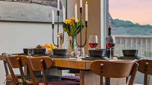 Uma mesa de jantar posta com velas, uma garrafa de vinho e uma saladeira de frutas.