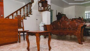Una habitación con una silla de madera, un sofá de madera, un armario de madera, suelo de mármol y una escalera.
