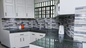 Una cocina con gabinetes blancos, encimera de granito, salpicadero de azulejos blanco y negro, y un lavamanos de acero inoxidable.