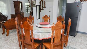 Un comedor con una mesa redonda, seis sillas de madera, un mantel rojo y un refrigerador negro al fondo.