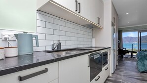 A modern kitchen with a black countertop, white cabinets, and a built-in oven. - Studio 5 - Waterfront Studio at HarbourLights (One Tree Point)