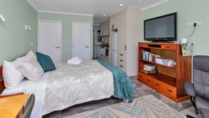 A bedroom with a bed, a television, a bookshelf, and a desk. - Studio 5 - Waterfront Studio at HarbourLights (One Tree Point)