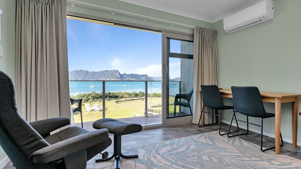 A room with a view of the sea, a table, two chairs, and an air conditioning unit. - Studio 5 - Waterfront Studio at HarbourLights (One Tree Point)