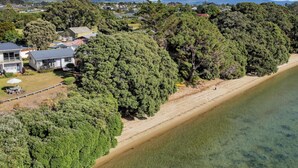 A coastal property with a beach, dense trees, and a house with a visible deck. - Studio 5 - Waterfront Studio at HarbourLights (One Tree Point)