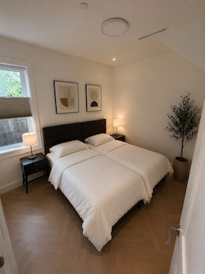 Ein Schlafzimmer mit Bett, Nachttischen, einem Fenster und einem Blumentopf.