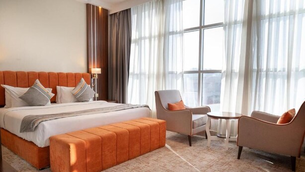 A hotel room with a large bed, a sitting area with two chairs, a small table, and a large window with curtains. - Rich Lobby Hotel (Ha'il)
