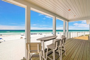 Eine überdachte Terrasse mit Blick auf den Strand, einem Tisch und Stühlen.