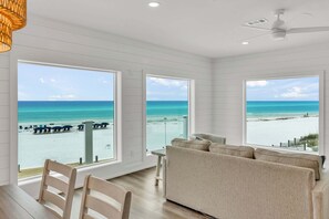Ein Zimmer mit großen Fenstern mit Blick auf einen Strand, einem Deckenventilator und einem Holzboden.