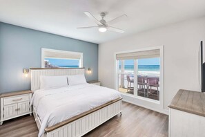 Ein Schlafzimmer mit Bett, Nachttischen, Deckenventilator und Fenster mit Meerblick.