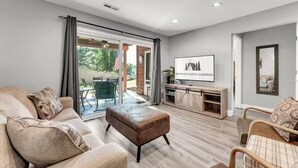 A modern living room with a sofa, ottoman, and a television mounted on the wall. - Indoor Pool, Hot Tub, PT Royale, Bunk Room, LAKE! (Branson)