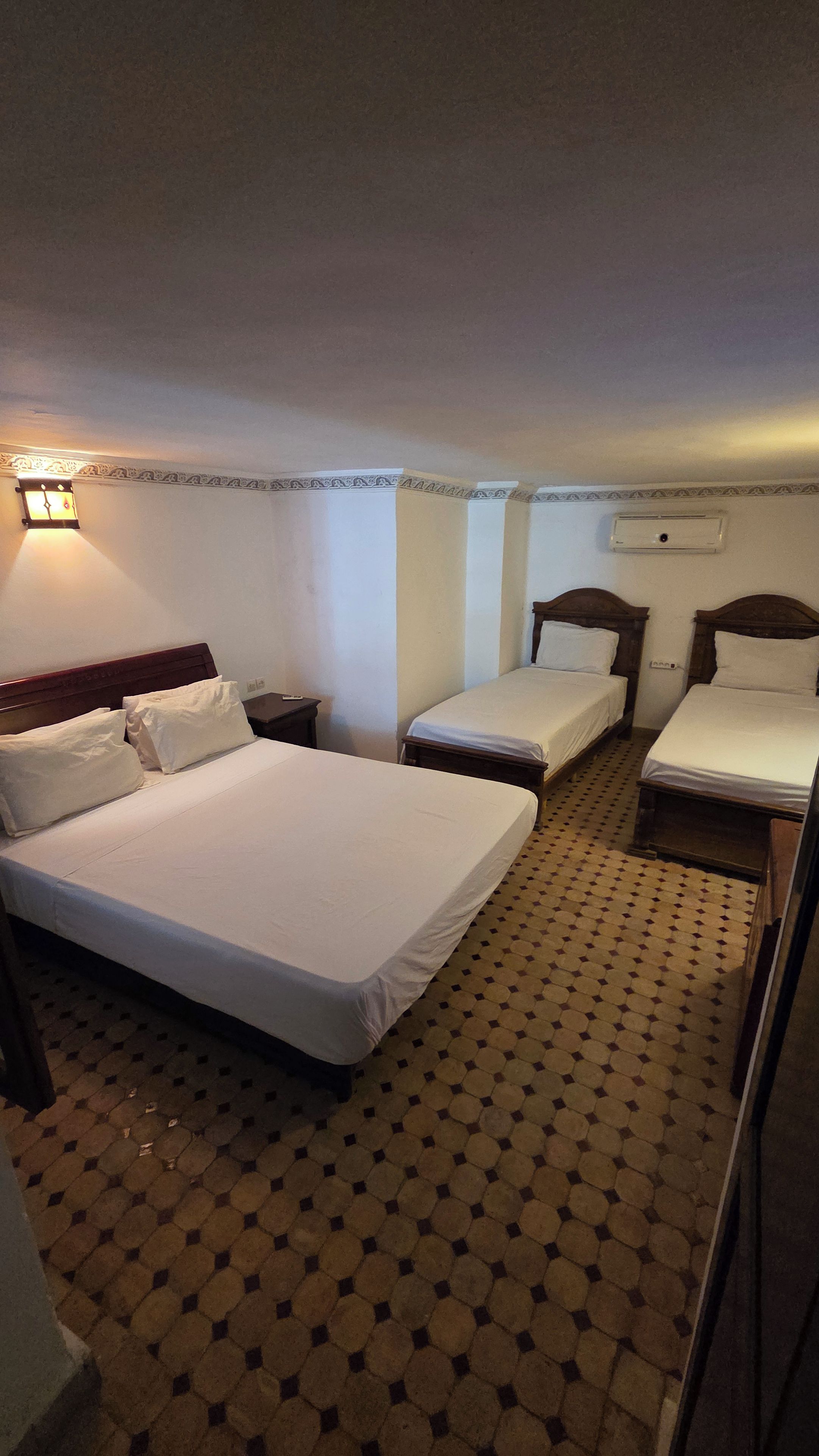 Une chambre d’hôtel avec trois lits, une table de chevet, une lampe et un sol à motifs.