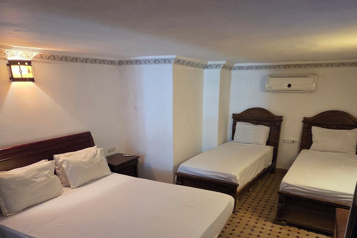 A hotel room with three beds, a nightstand, a lamp, and a patterned floor.