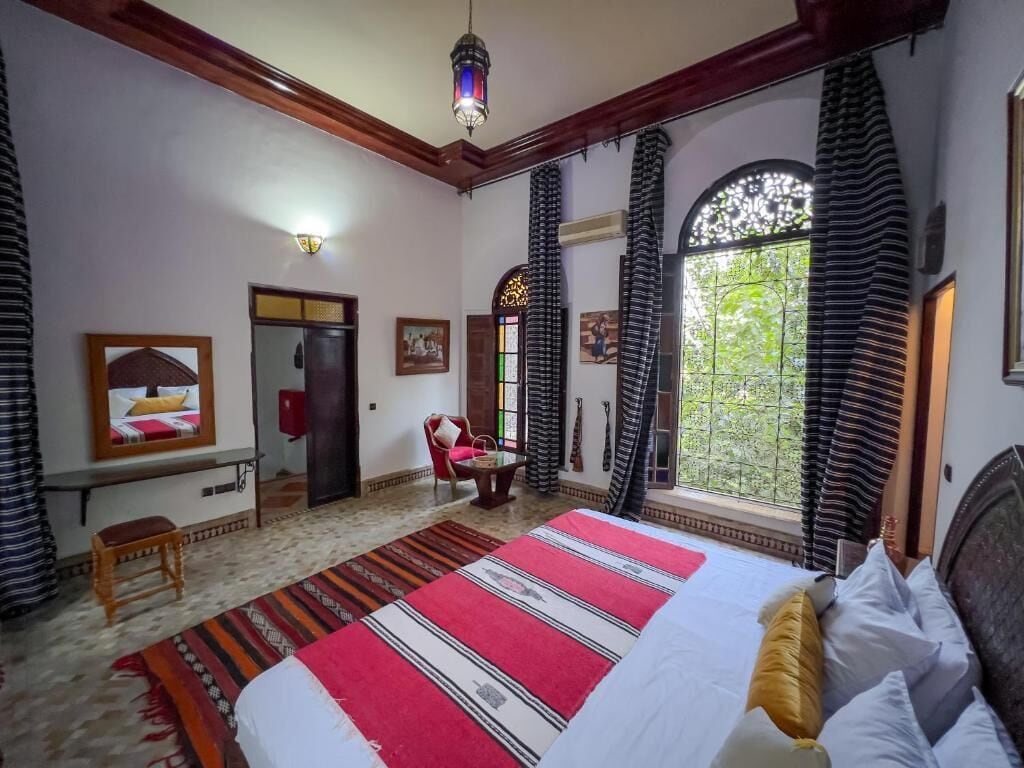 A bedroom with a large bed, a desk, a chair, and a window with curtains.