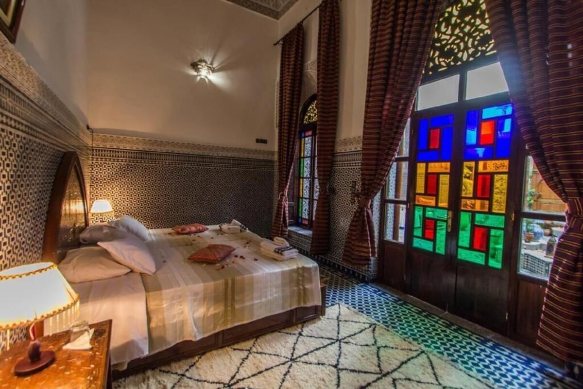 Una stanza con un letto, una finestra con vetrate colorate e un pavimento decorato.