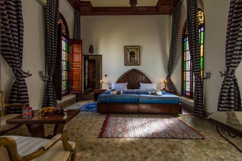 A room with a bed, a wooden table, a chair, and a patterned rug.