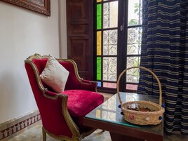 Una silla tapizada de rojo con un cojín, una mesa de vidrio con una cesta de mimbre y una reja decorativa de hierro con vidrios de colores.
