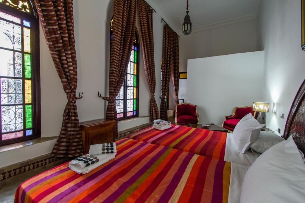 A hotel room with a large bed, a red chair, a small table, and a window with curtains.