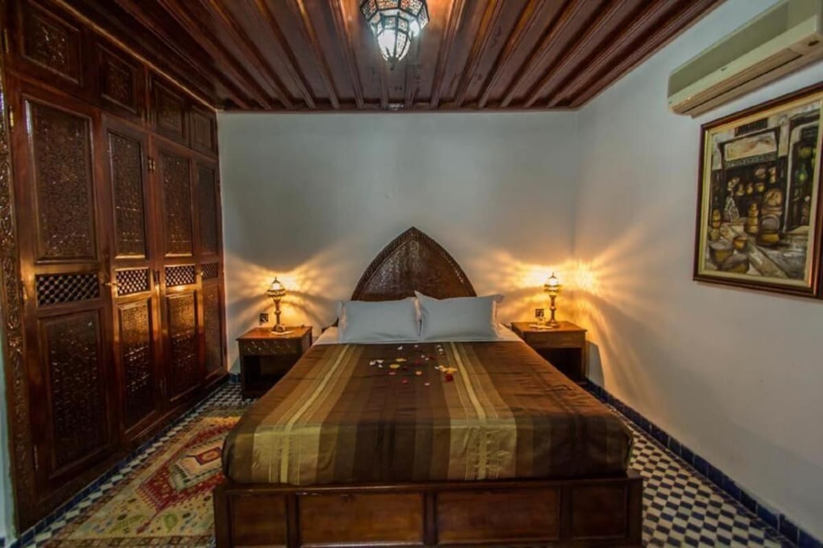 Una stanza con un letto, due comodini con lampade, un tappeto decorato e un soffitto ornamentale.