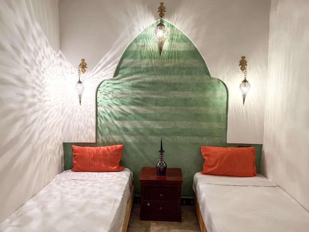 Una habitación con dos camas, una mesita de noche y un elemento decorativo en forma de arco verde.