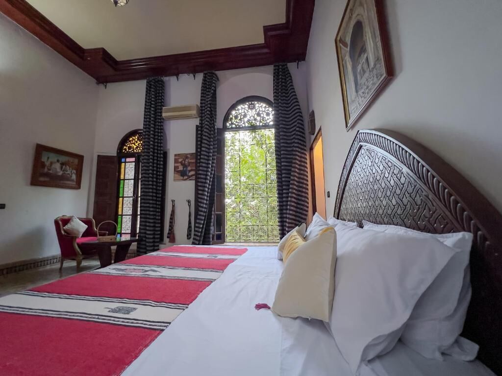 A hotel room with a large bed, a chair, a desk, a window with curtains, and a framed picture on the wall.
