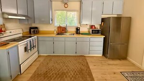 Een keuken met grijze kastjes, een roestvrijstalen koelkast, een magnetron, een fornuis en een raam met jaloezieën.