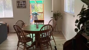 Een eetruimte met een ronde tafel en stoelen, een plafondlamp en uitzicht door een deur op een buitenruimte.