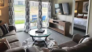 Habitación de hotel con sofá, una mesa de centro de vidrio, televisión, cama y vistas al exterior.