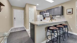 Una cocina con una isla central, taburetes de bar, microondas y refrigerador.