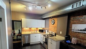Una cocina moderna con armarios blancos, electrodomésticos de acero inoxidable y una pared decorada con ladrillo.
