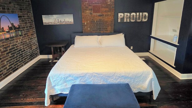 Un dormitorio con cama, ventilador de techo, pared de ladrillo y un espejo grande.