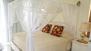 A bed with a canopy, two pillows, a bedside table with a lamp, and a nightstand. - Unit 6 Coast Luxury Town Homes  Newly Refurbished (Rodney Bay)