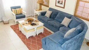 A living room with a blue sofa, a white armchair, a coffee table, and a patterned rug. - Unit 6 Coast Luxury Town Homes  Newly Refurbished (Rodney Bay)