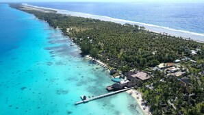 Luchtbeeld van een landgoed aan de kust, met een pier die uitsteekt in het turquoise water, omringd door weelderige begroeiing en een strand.