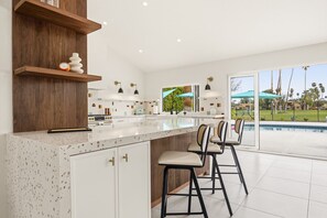 Eine moderne Küche mit einer großen Kochinsel, Barhocker und Blick auf einen Swimmingpool.