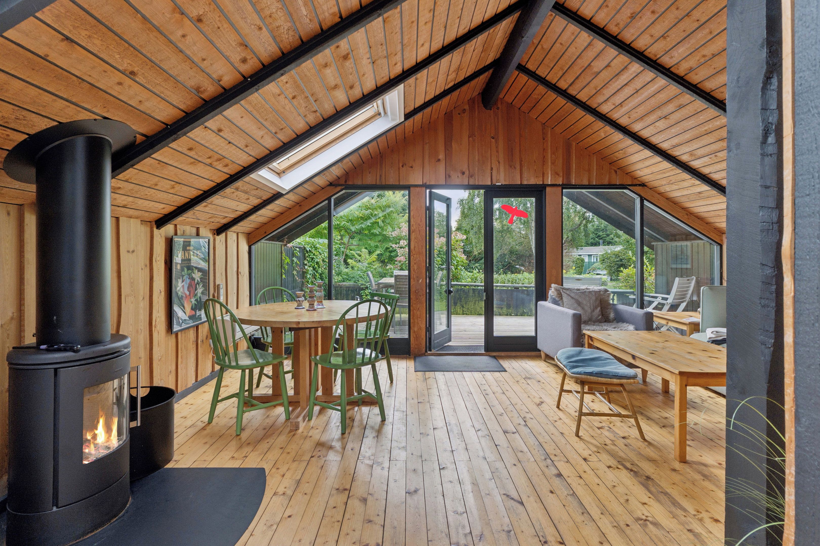 A cozy interior with a wooden ceiling, a central table with chairs, a sofa, and a fireplace.