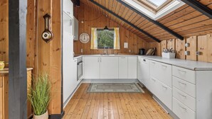 A kitchen with wooden walls, a skylight, a clock, and a plant. - Charming holiday home near beach and town (Dronningmølle)