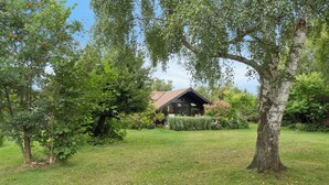 A house with a sloped roof, surrounded by a grassy yard and trees. - Charming holiday home near beach and town (Dronningmølle)