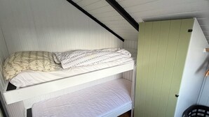 Een stapelbed met een onderbed, een groene kast en een zwarte prullenbak in een kamer met houten vloeren.