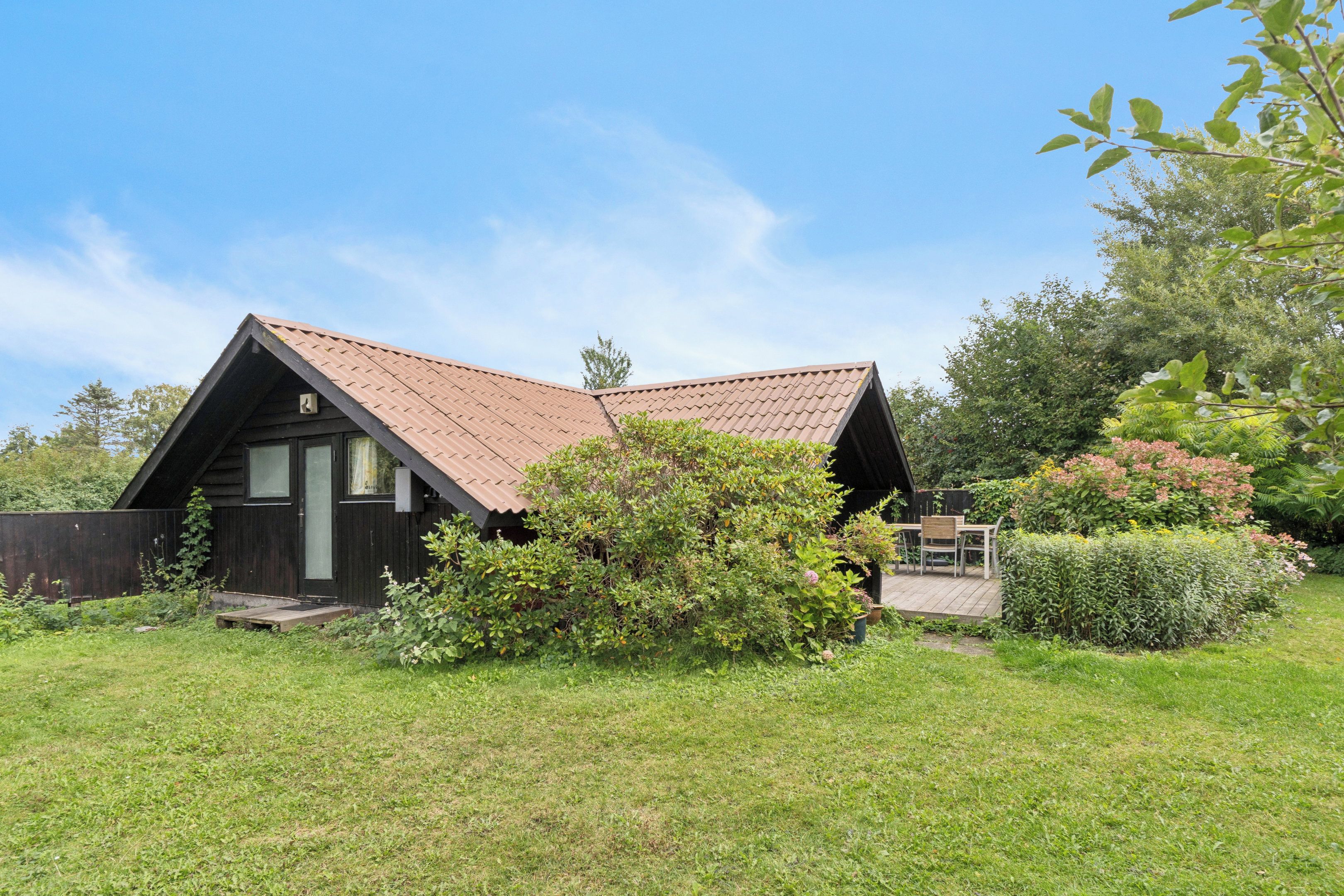 Une petite maison de plain-pied, dotée d’un toit en pente, entourée d’un jardin bien entretenu et agrémentée d’une terrasse en bois.