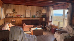 A cozy living room with a wooden ceiling, a sofa, a chair, a small table, and a view of the outdoors. - South shore time capsule (Canoe Cove)