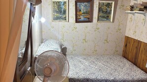 A room with a bed, a standing fan, and two framed paintings on the wall. - South shore time capsule (Canoe Cove)