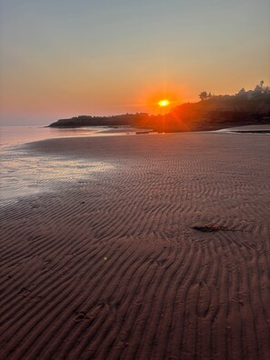 A beach with a sunset, sandy terrain, and a distant shoreline.
